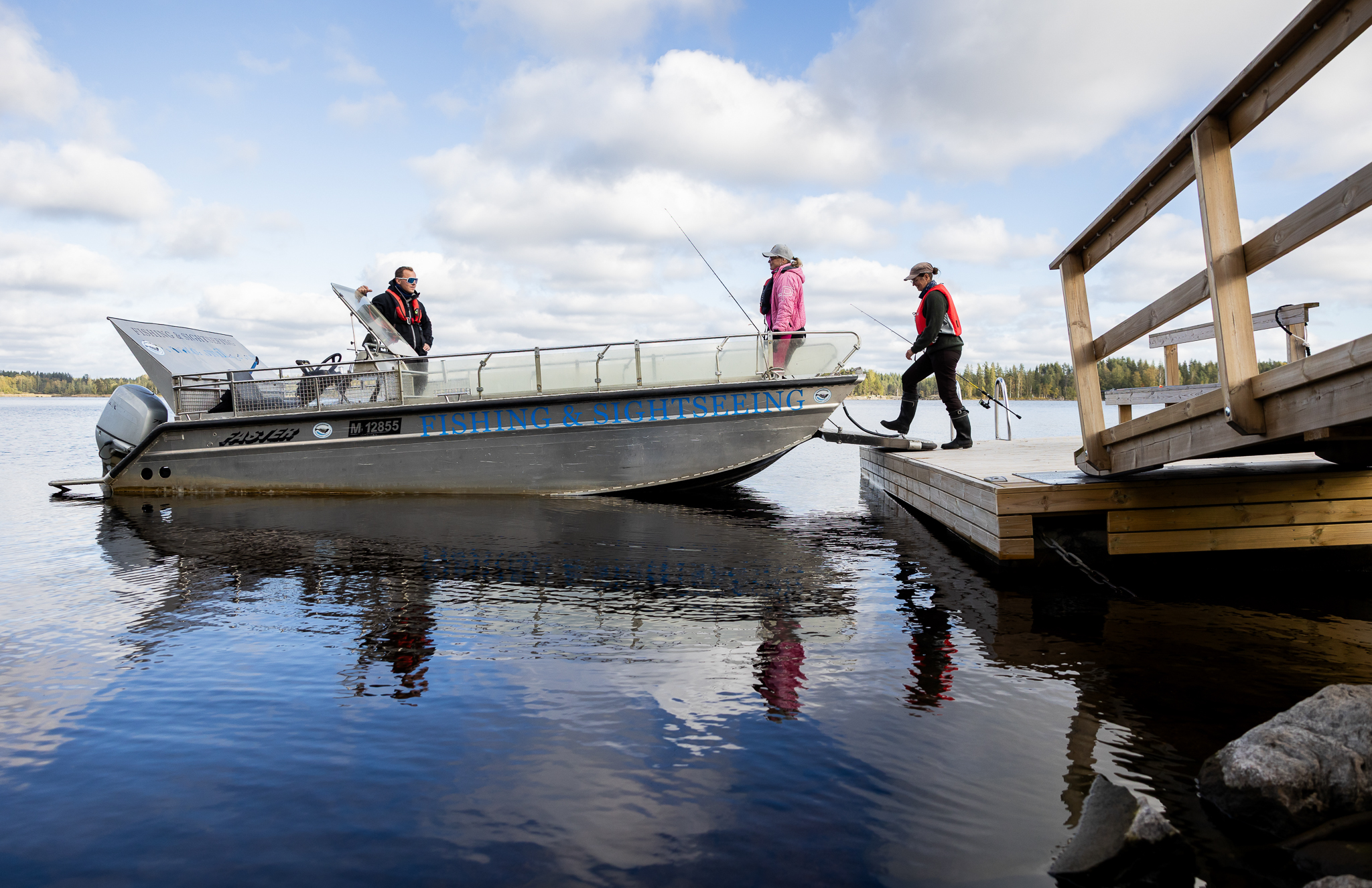 Ihmisiä noisemassa esteettömän veneen kyytiin mökin laiturilta
