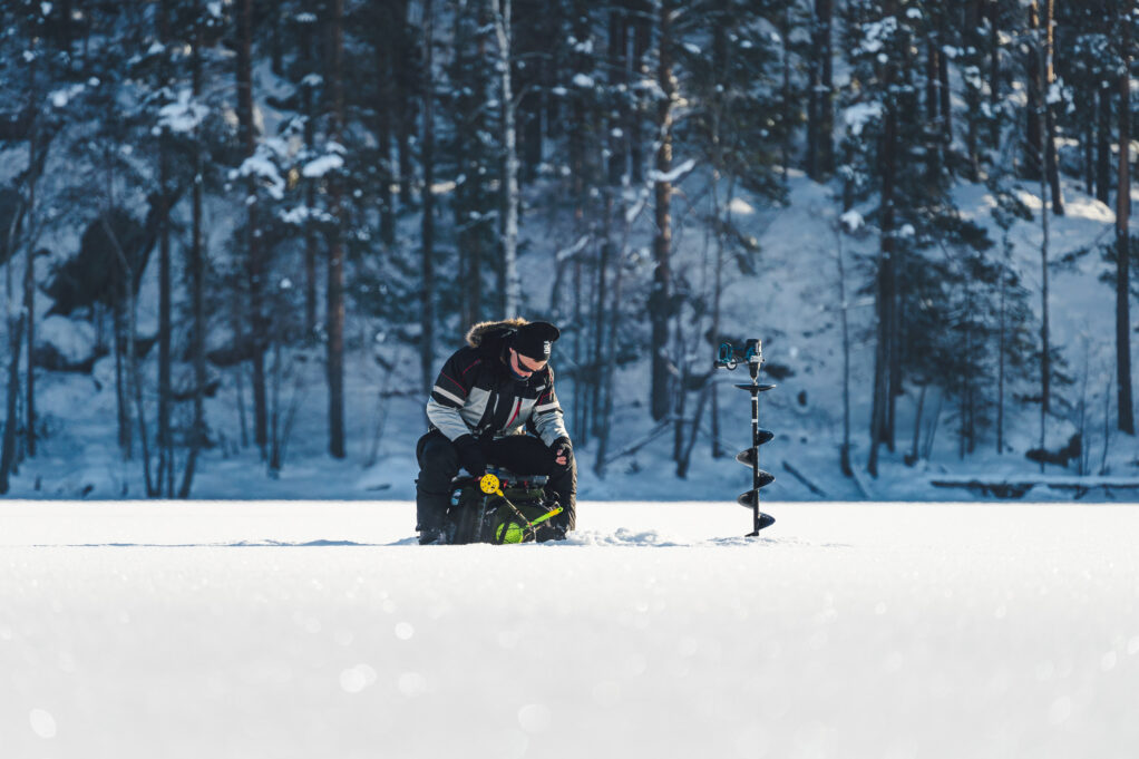 man sitting and ice fishing in a snowy winter landscape