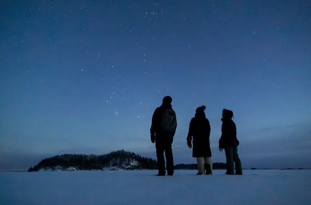 Three persons standing on the ice watching the stars in the sky